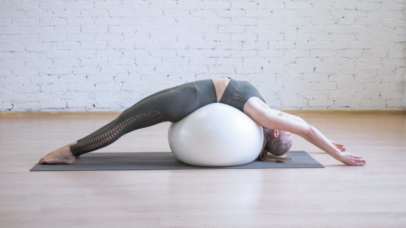 Mujer estirando la espalda usando balón de pilates blanco en estudio pilates